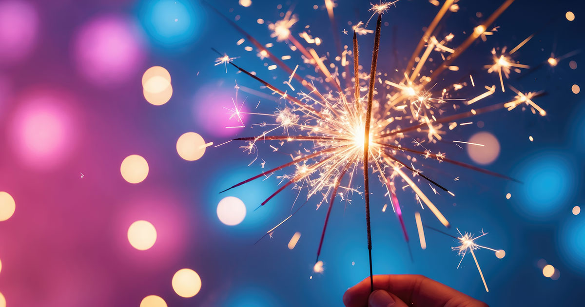 Person holding sparkler during fireworks on the fourth of july